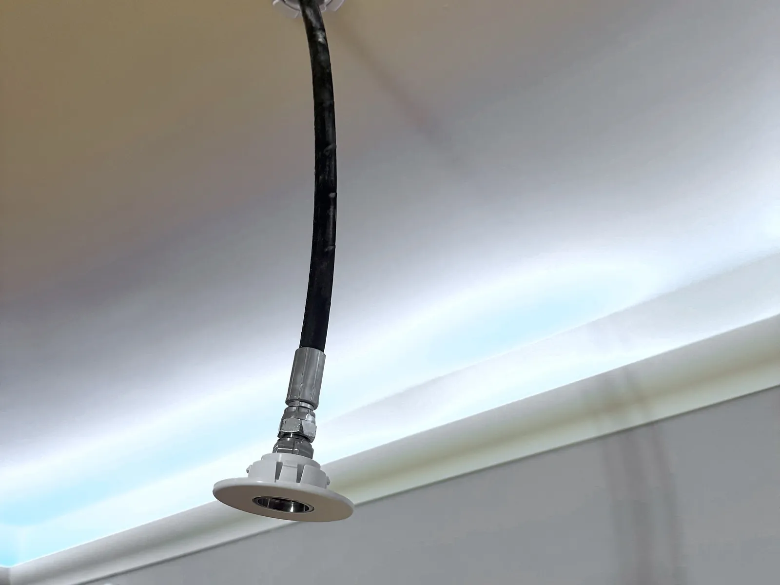 Water mist nozzle on its flexible feed hose, fitted at first fix before the ceiling is closed